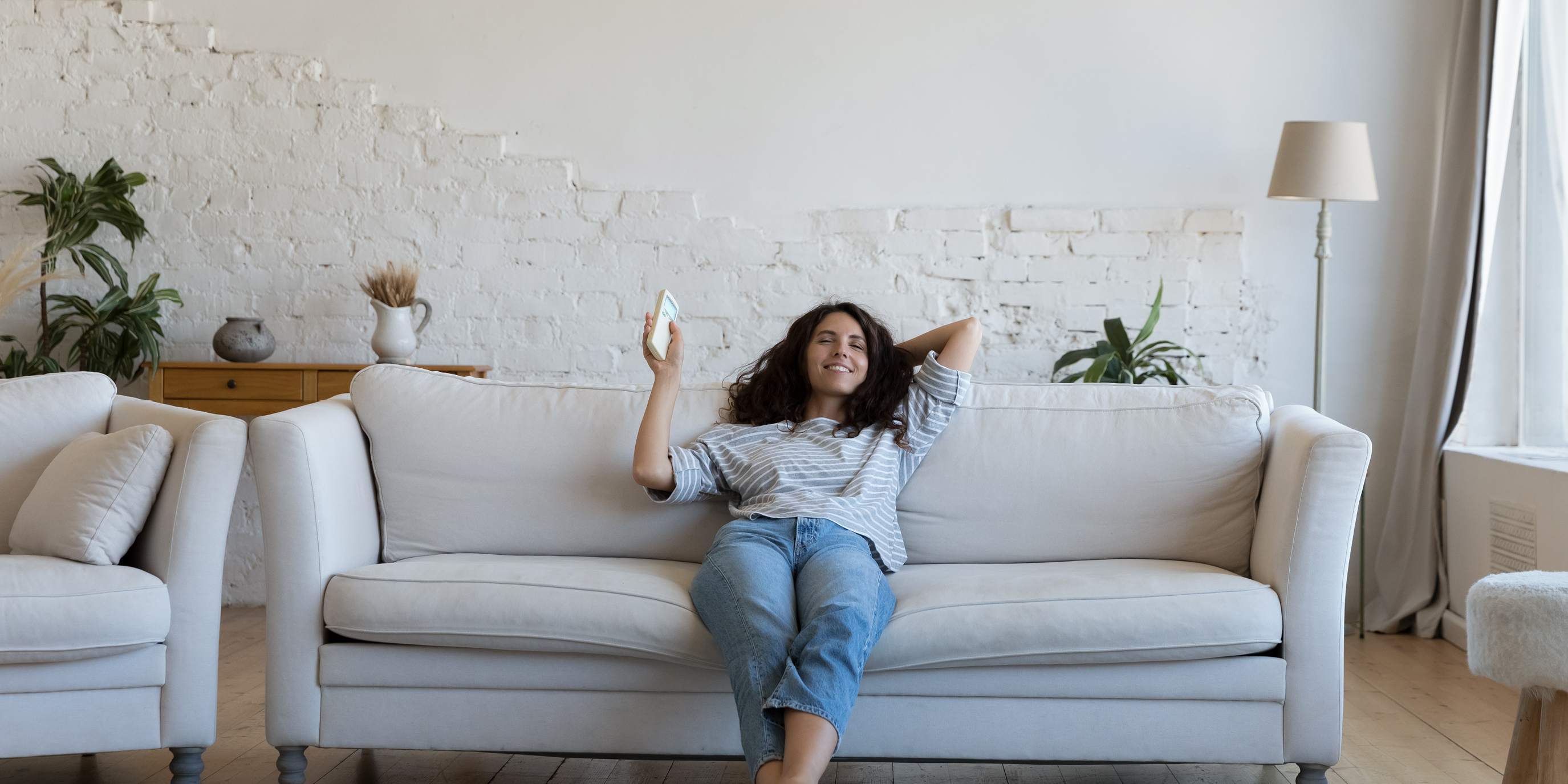 A woman sits on a couch under an air conditioner.